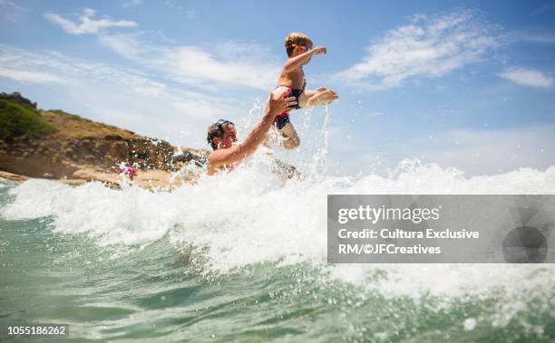 man throwing son into ocean wave, calvi, corsica, france - happy famille france photos et images de collection