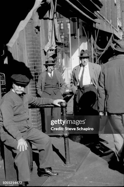 View of several men, one seated and two others leaning with their hands in their pockets, near a unidentified café in Manhattan's Lower East Side,...