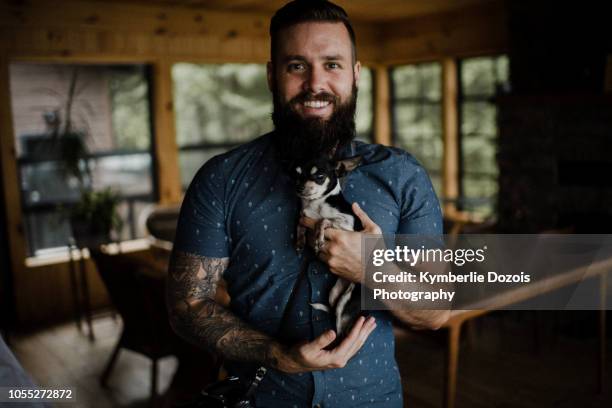 young man holding pet dog in living room, portrait - chihuahua dog stockfoto's en -beelden