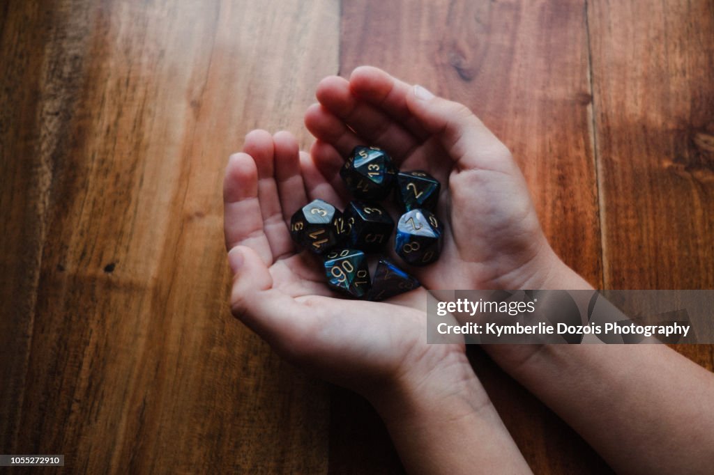 Girl with cupped hands at table holding role playing dice, close up