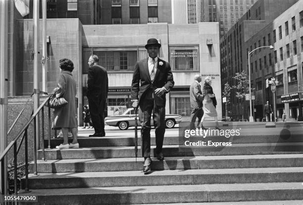 American heavyweight boxer Muhammad Ali pictured wearing pinstripe trousers, suit jacket, spats and bowler hat on steps opposite the Rockefeller...