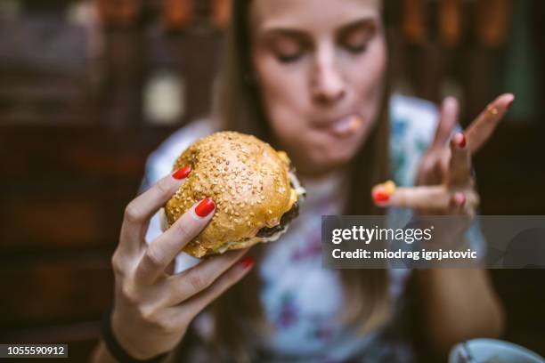 woman enjoying delicious burger - lamber imagens e fotografias de stock