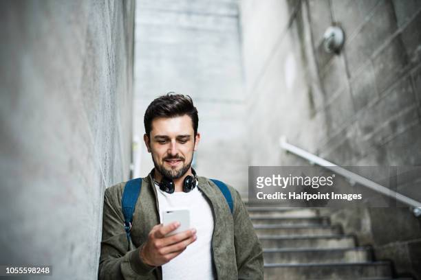 a young man with headphones and smartphone standing on the stairs, listening to music. - street style phone stock pictures, royalty-free photos & images