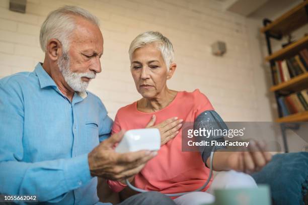 lovely senior couple measuring blood pressure - sick wife stock pictures, royalty-free photos & images