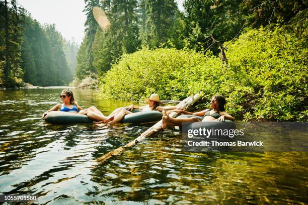 smiling female friends hanging out in inner tubes on river on summer afternoon - native river stock-fotos und bilder