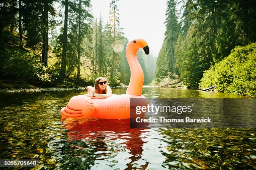 Portrait of laughing woman floating down river on inflatable pink flamingo Portrait of laughing woman floating down river on inflatable pink flamingo
