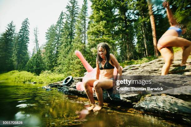 smiling woman preparing to jump into river with friends on summer afternoon - native river stock-fotos und bilder