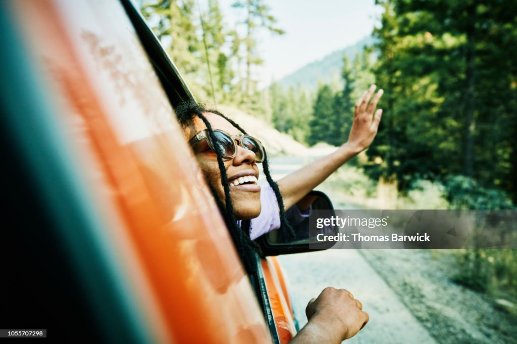 Smiling woman with head and hand out of car window enjoying view of mountains