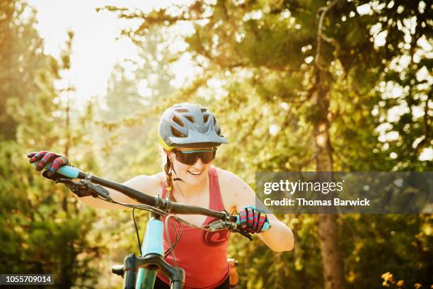 smiling female mountain bike pushing bike uphill during ride on summer evening - トレーニンググローブ ストックフォトと画像
