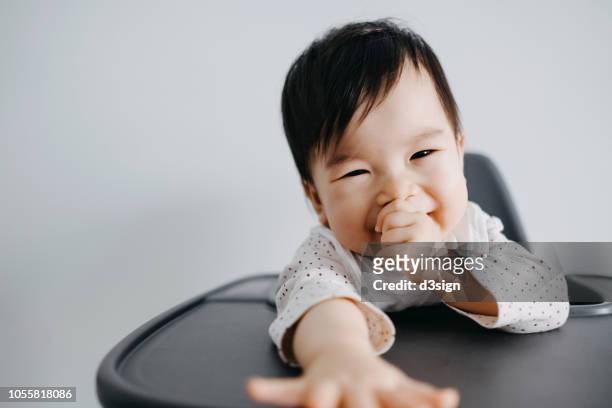 cute baby girl sitting on high chair sucking her thumb and smiling joyfully - suck stock pictures, royalty-free photos & images