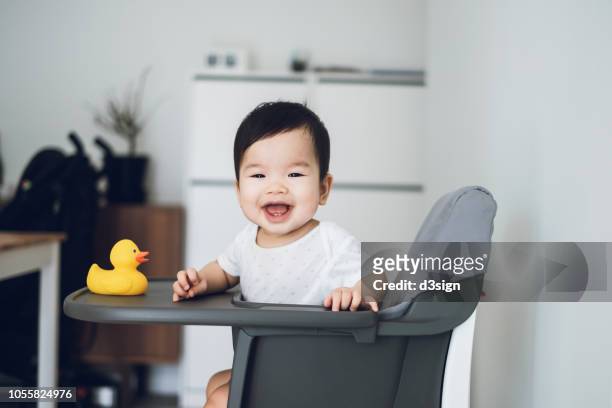 joyful baby smiling happily and playing with yellow rubber duck in high chair - bébé grimace photos et images de collection