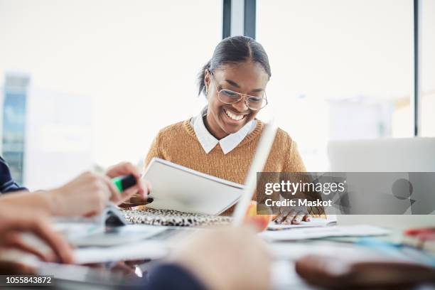 smiling woman studying while sitting with friends at table in university cafeteria - black literature stock pictures, royalty-free photos & images