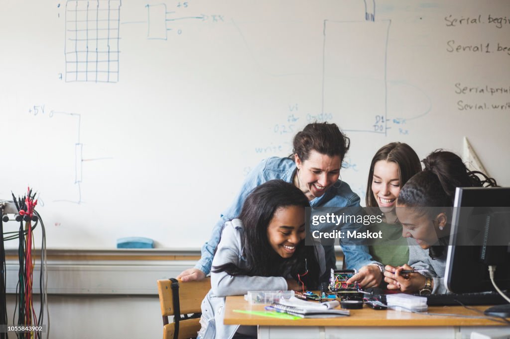 Smiling female teacher and high school teenage students preparing robot on desk in classroom