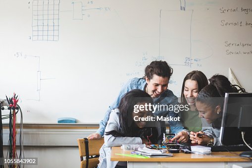 Smiling female teacher and high school teenage students preparing robot on desk in classroom Smiling female teacher and high school teenage students preparing robot on desk in classroom