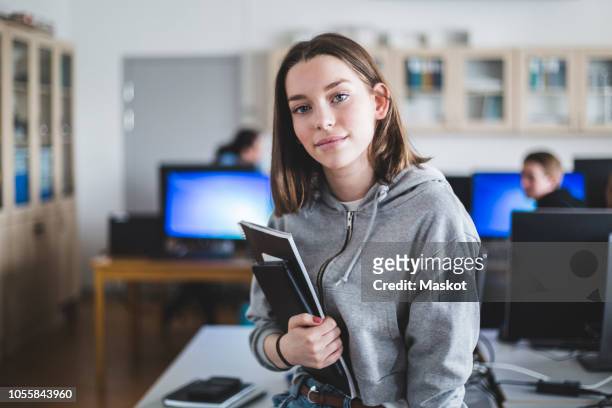 portrait of confident high school female student with books in classroom - high school portrait stock-fotos und bilder