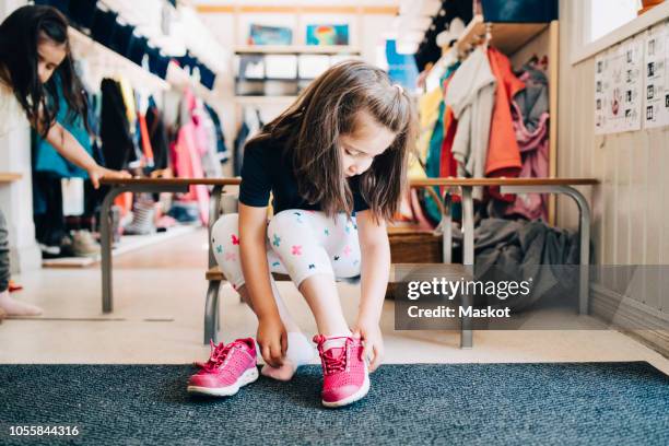 full length of girl sitting on bench wearing shoes in cloakroom at preschool - girls shoes bildbanksfoton och bilder