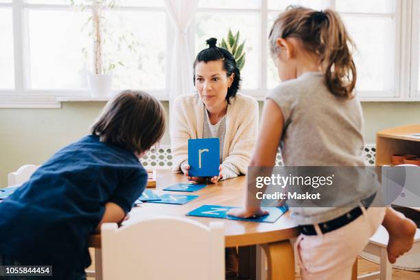 confident female teacher holding letter r in front of students at table in classroom - letter r stock-fotos und bilder