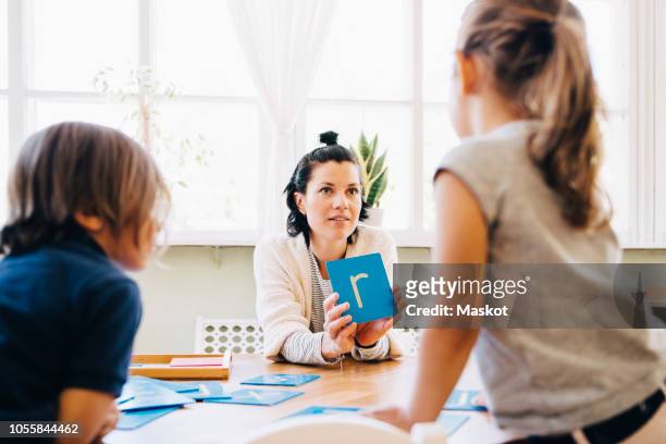 confident female teacher showing letter r to students at table in classroom - letter r stock pictures, royalty-free photos & images