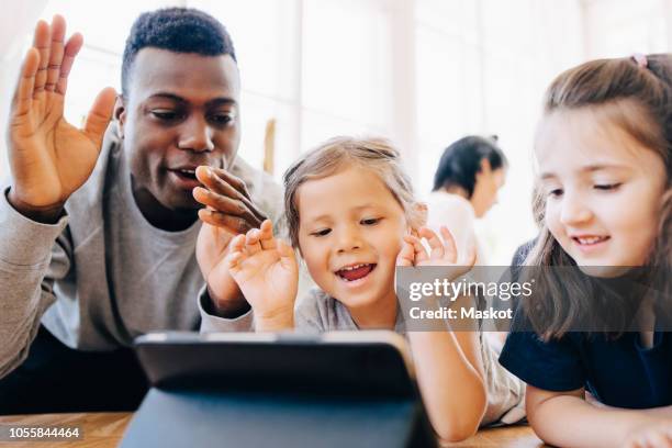 playful teacher and female students looking at digital tablet in classroom - nursery school building stock pictures, royalty-free photos & images