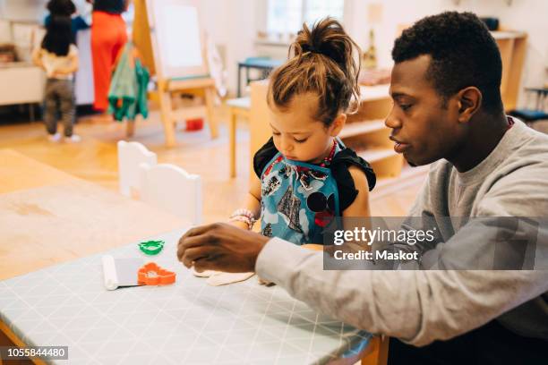 mid adult male teacher playing with girl at table in child care classroom - child care stock pictures, royalty-free photos & images