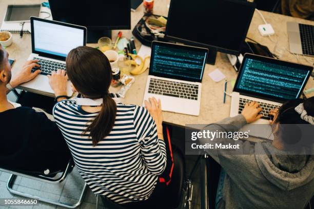 high angle view of young multi-ethnic computer programmers coding on laptops at desk in small office - computer programmer ストックフォトと画像