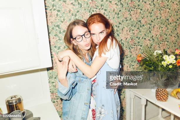 portrait of young redhead woman embracing female friend showing horn sign at home - floral pattern jacket stock-fotos und bilder