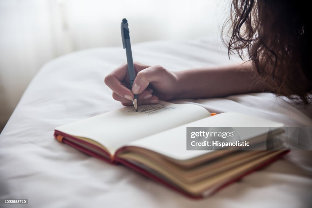 Unrecognizable woman lying on her bed while drawing on her notebook