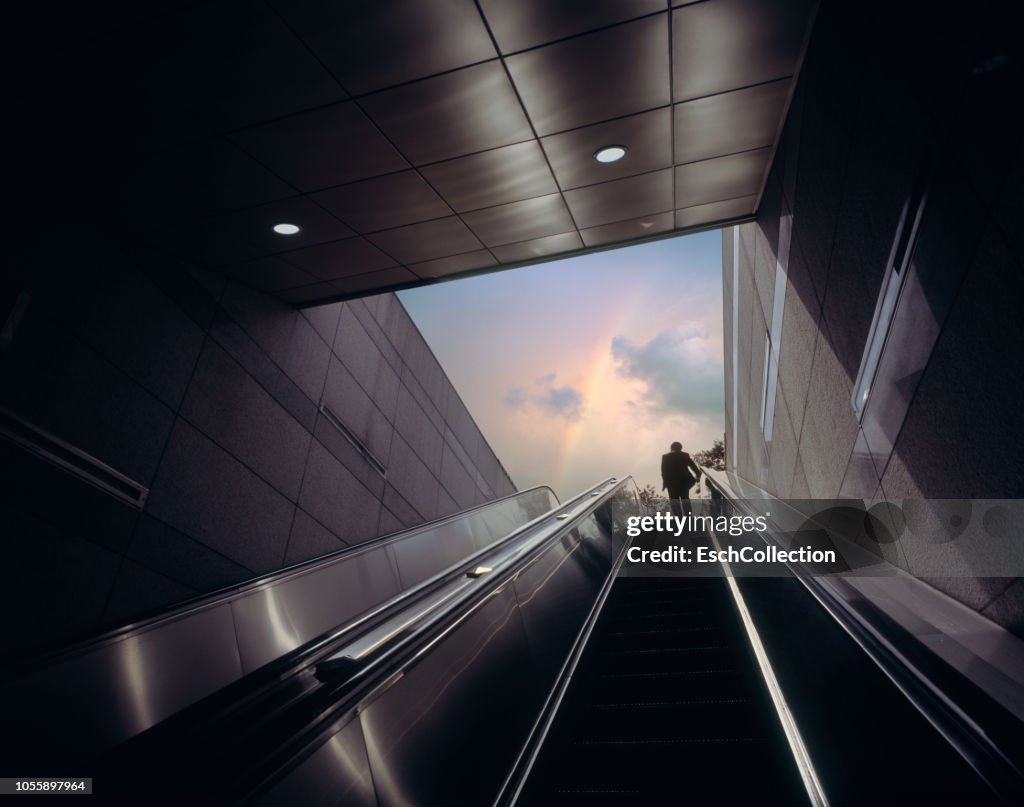Businessman on escalator moving towards sky with rainbow