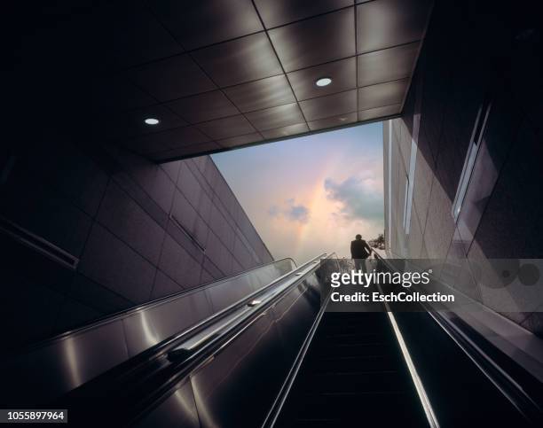 businessman on escalator moving towards sky with rainbow - erwartung stock-fotos und bilder