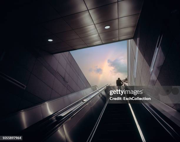 businessman on escalator moving towards sky with rainbow - success story photos et images de collection