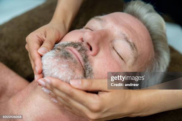 hombre adulto, recibir un masaje facial en un spa - indulgence fotografías e imágenes de stock