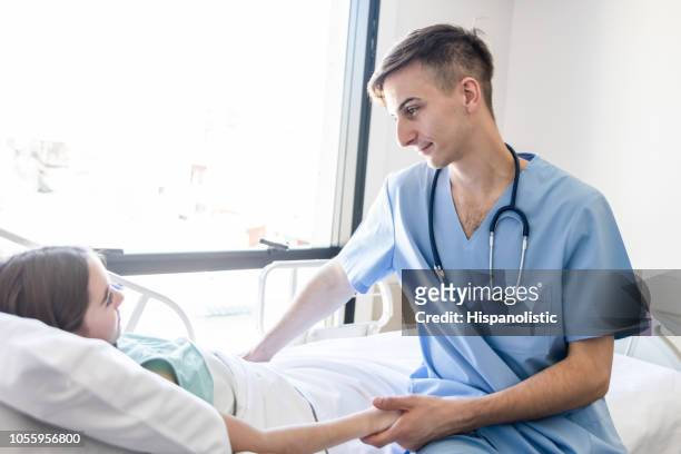 sweet male nurse holding a little girls hand while she is lying down on hospital bed - patient lying down stock pictures, royalty-free photos & images