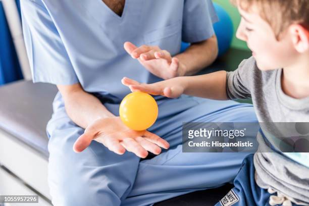 onherkenbaar ergotherapeut met weinig mannelijke patiënt doen de oefening van een hand met een kleine bal - medicine ball stockfoto's en -beelden