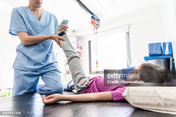 unrecognizable physical therapist helping a little girl stretch her leg while she is lying on gurney - leg stretch girl stock pictures, royalty-free photos & images