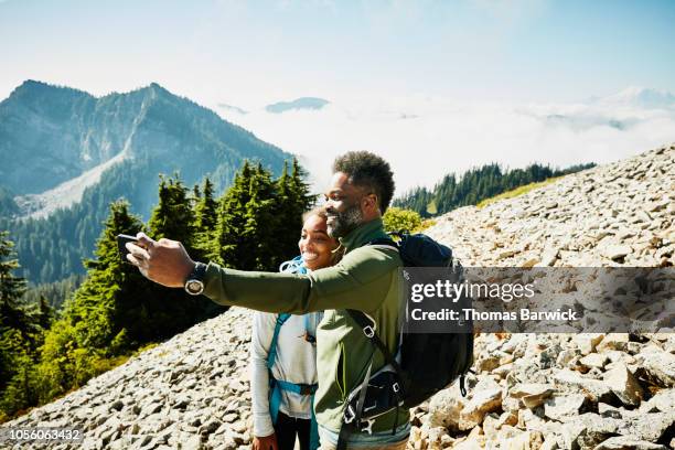 smiling father and daughter taking selfie with smart phone during hike in mountains - travel16 stock pictures, royalty-free photos & images