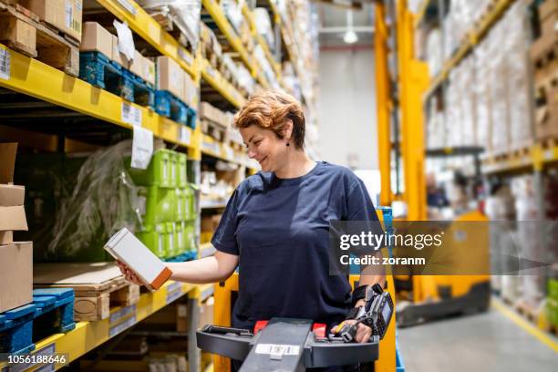 mid adult woman holding cardboard box in warehouse - shelf strip stock pictures, royalty-free photos & images