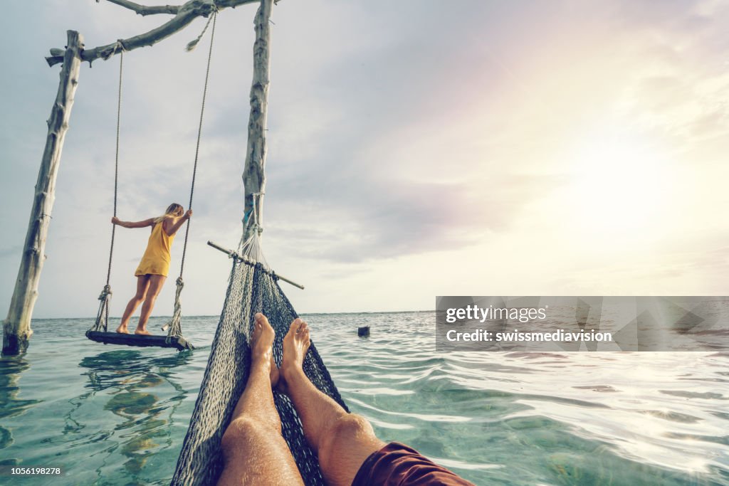 Junges paar am Strand am Meer, schöne und idyllische Landschaft schwingen. Die Leute reisen Romantik Urlaub Konzept. Persönlichen Sicht der Mann am Meer-Hängematte und Freundin auf Meer Schaukel.