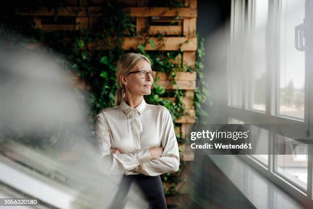 businesswoman in green office looking out of window - conservazione ambientale foto e immagini stock