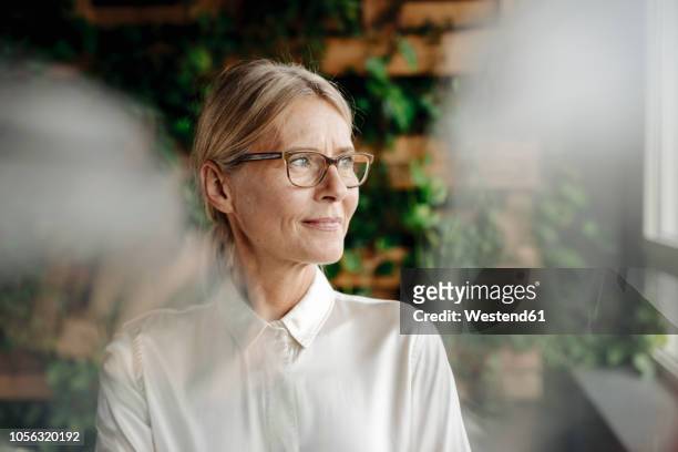 businesswoman in green office looking out of window - vrouw 50 jaar stockfoto's en -beelden