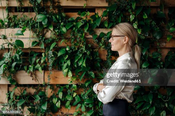 businesswoman at wall with climbing plants - greenside stock-fotos und bilder