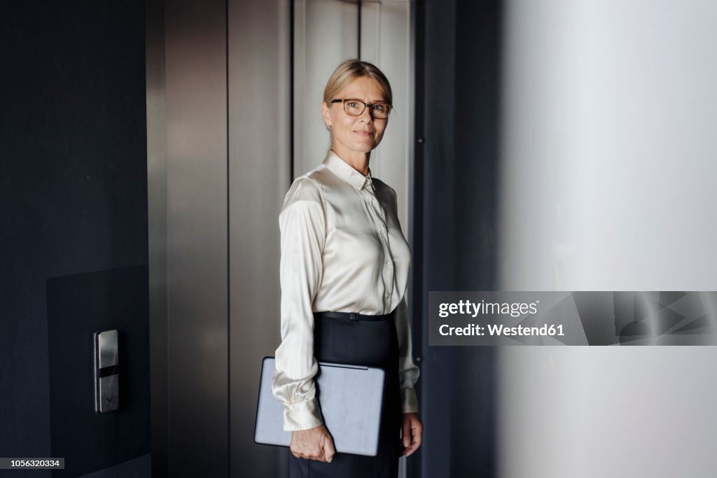 Confident businesswoman in office holding laptop