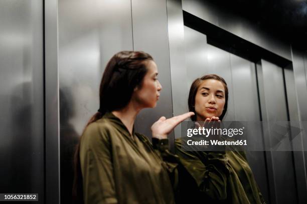 young woman looking in mirror in elevator blowing a kiss - autoimagem imagens e fotografias de stock