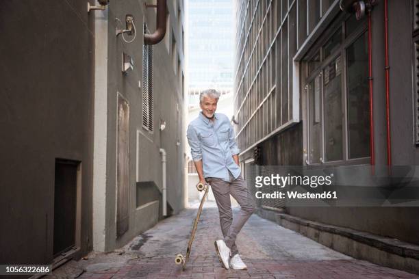 mature man with longboard in an alley - luta fysisk ställning bildbanksfoton och bilder