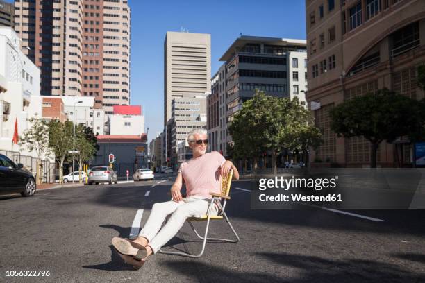 mature man sitting on chair in the street, wearing sunglasses - foldable stockfoto's en -beelden