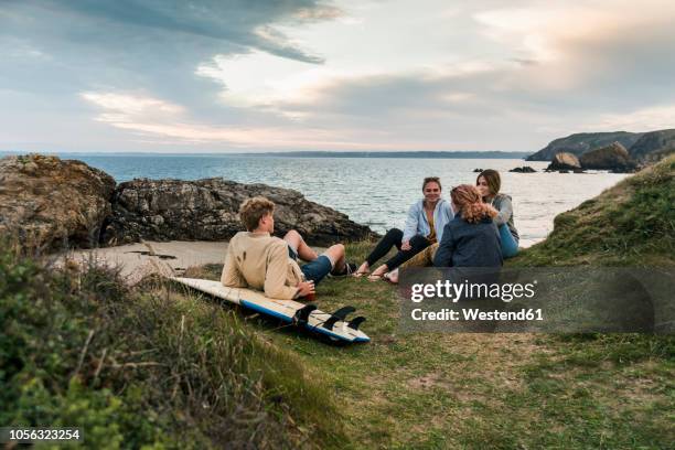 happy friends with surfboard socializing at the coast at sunset - bretagne - fotografias e filmes do acervo