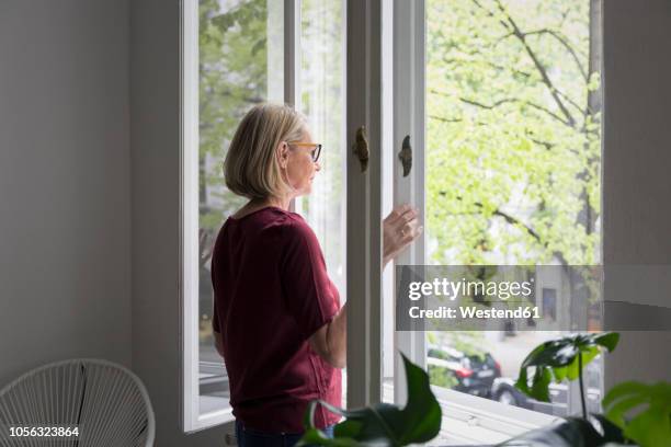 mature woman at home opening the window - open window stock pictures, royalty-free photos & images