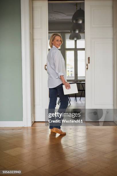 smiling mature woman holding tablet at home - sliding door stock-fotos und bilder