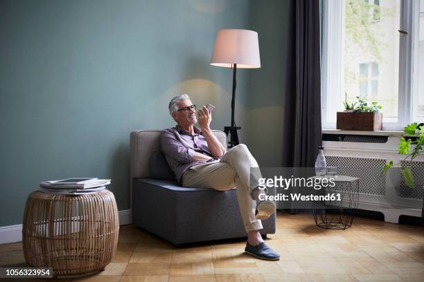 mature man using cell phone at home - wohnzimmerlampe stock-fotos und bilder