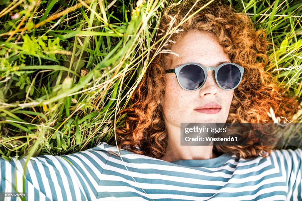 Portrait of young woman relaxing on a meadow wearing sunglasses