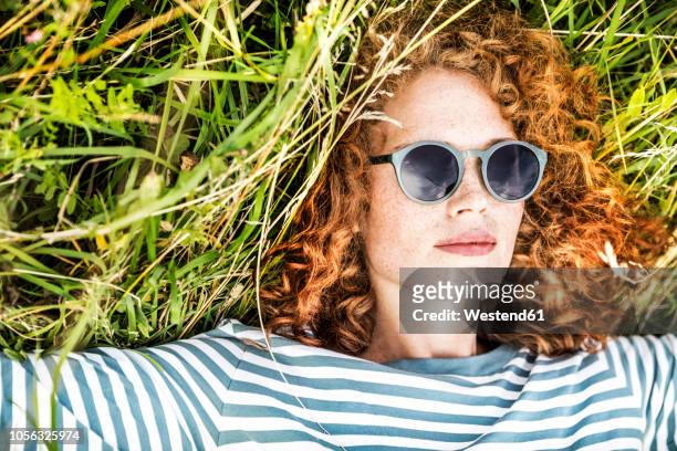 portrait of young woman relaxing on a meadow wearing sunglasses - sunglasses woman stock pictures, royalty-free photos & images